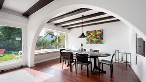 Un coin repas avec une table dressée pour quatre personnes, un luminaire suspendu et un tableau abstrait aux couleurs vives accroché au mur.
