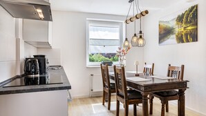 A modern kitchen with a dining area, a window with blinds, and a painting on the wall. - Grimms Suite Apartment (Kassel)