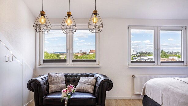A room with a leather sofa, a wooden coffee table, and a view through large windows. - Grimms Suite Apartment (Kassel)
