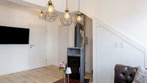 A living room with a fireplace, a sofa, a coffee table with a vase and lamp, and pendant lights. - Grimms Suite Apartment (Kassel)