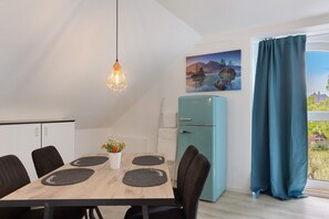 Un comedor con una mesa de madera, sillas negras, un refrigerador verde azulado y un cuadro en la pared.