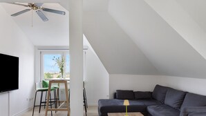 A modern living room with a sofa, a small table, a TV, and a ceiling fan. - Herkules Suite Apartment in Kassel (Kassel)