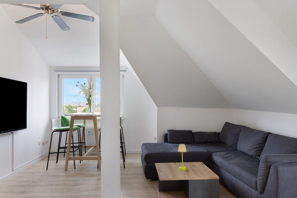 Una sala de estar moderna con un sofá, una mesita, un televisor y un ventilador de techo.