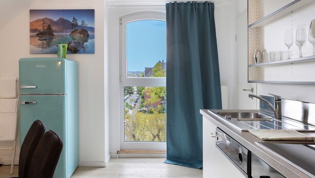 A kitchen with a view of a tree-lined street, a blue refrigerator, and a stainless steel sink. - Herkules Suite Apartment in Kassel (Kassel)