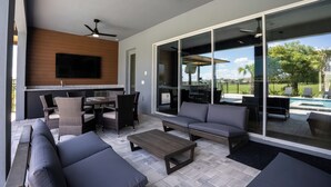 A modern outdoor living area with a sofa, chairs, a coffee table, and a TV mounted on a wall. - Luxury Golf Estate with Simulator, Bowling, Sauna (Reunion)