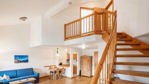 A spacious living area with a wooden staircase, a blue sofa, and a dining area.
