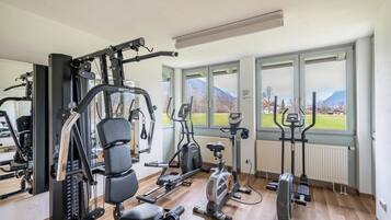 A gym with various exercise equipment, large windows with a view of mountains, and a wooden floor.