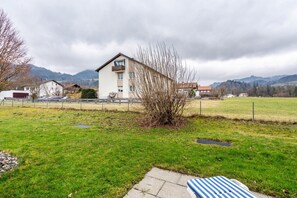 A residential area with a house, a grassy field, and mountains in the background. - Apartment 'Brünnstein Room 11' with Pool, Shared Garden, and Sauna (Oberaudorf)