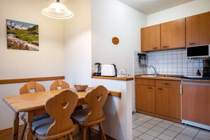 Une cuisine avec des meubles en bois, une table à manger avec des chaises, un tableau au mur et un luminaire.