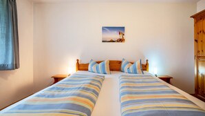 A double bed with striped bedding, a wooden headboard, two bedside tables with lamps, a small wall-mounted picture, and a wooden wardrobe.