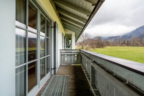 Une véranda couverte avec de grandes fenêtres, une terrasse en bois et une vue sur un champ verdoyant et des montagnes.