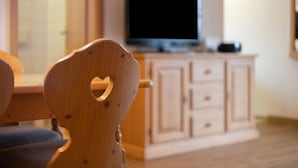 A wooden chair with a heart-shaped cutout, a television on a stand, and a wooden cabinet in a room.