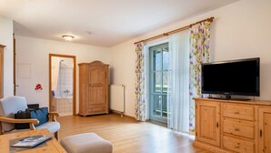 A room with a wooden cabinet, a television, a chair, a table, and a window with curtains.