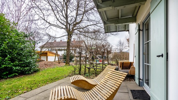 A curved wooden bench outside a building with a door and windows.