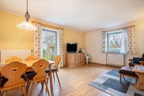 A room with a dining table, chairs, a television, and a sofa.