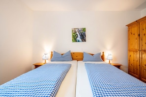 A double bed with checkered bedding, two bedside tables with lamps, a wooden wardrobe, and a framed picture on the wall.