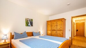 A double bed with checkered bedding, a wooden wardrobe, a nightstand with a lamp, and a framed picture on the wall.