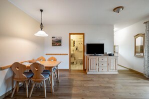 A dining area with a wooden table and chairs, a television on a cabinet, and a bathroom visible through an open door.