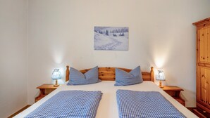Uma cama de casal com roupa de cama xadrez, cabeceira de madeira, duas luminárias de cabeceira, um quadro na parede e um guarda-roupa de madeira.