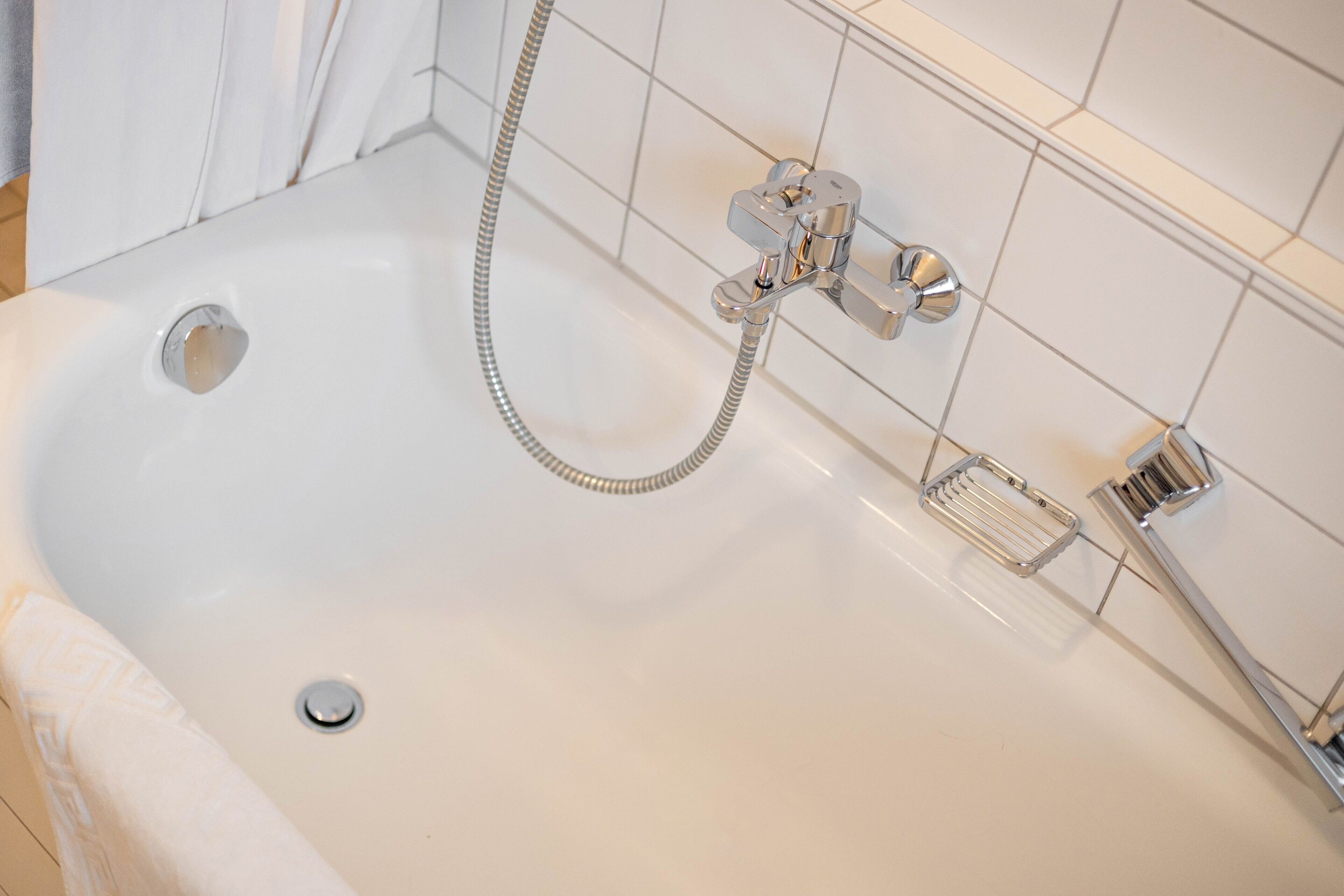 Een witte badkuip met een handdouche en een inbouw kraan.
