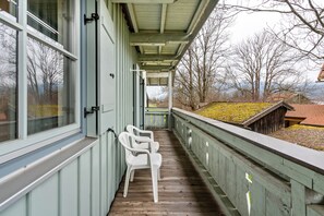 A covered porch with a wooden floor, white plastic chairs, and a view of a mountain and bare trees. - Studio 'Brünnstein-Zimmer 40' with Pool, Shared Garden and Sauna (Oberaudorf)