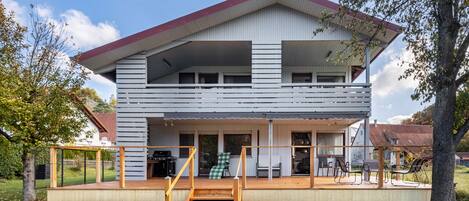 A two-story house with a wooden deck, a staircase, and a covered outdoor area with seating.