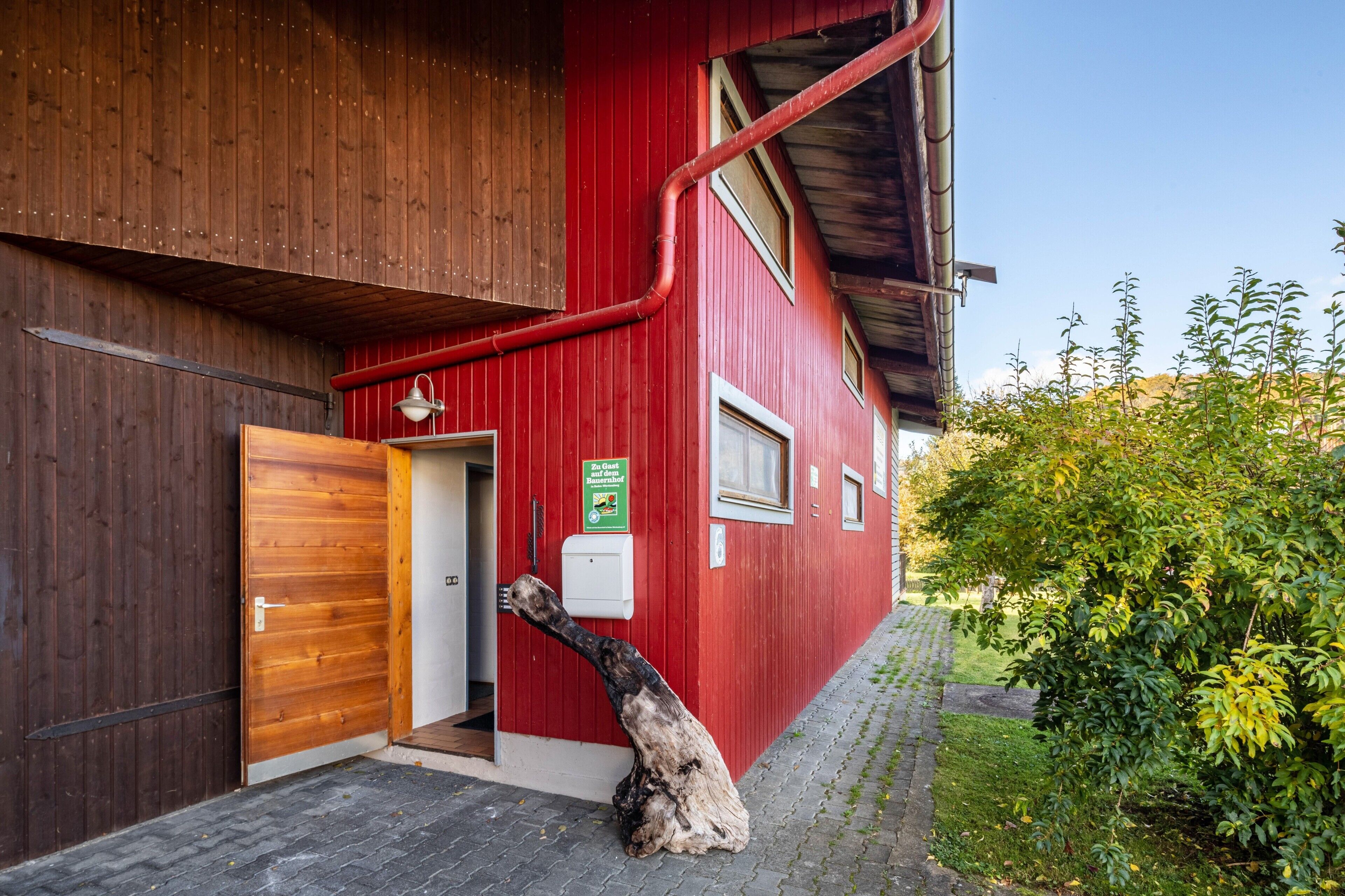 Ein rotes Gebäude mit Holztür, einem Schild und einer Rohrleitung an der Seite.
