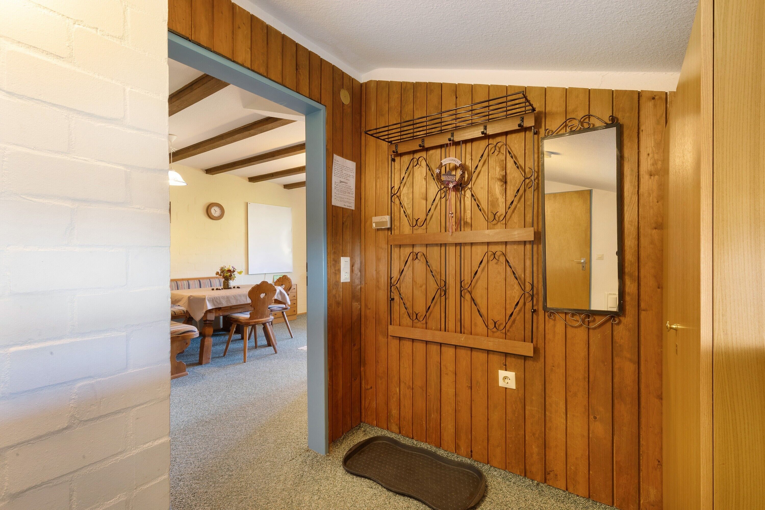 Quarto com paredes de madeira, um espelho, uma porta e um tapete pequeno.