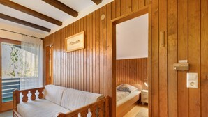 Ett rum med träpanel på väggarna, en säng, en soffa, ett fönster med gardiner och en väggmonterad termostat.