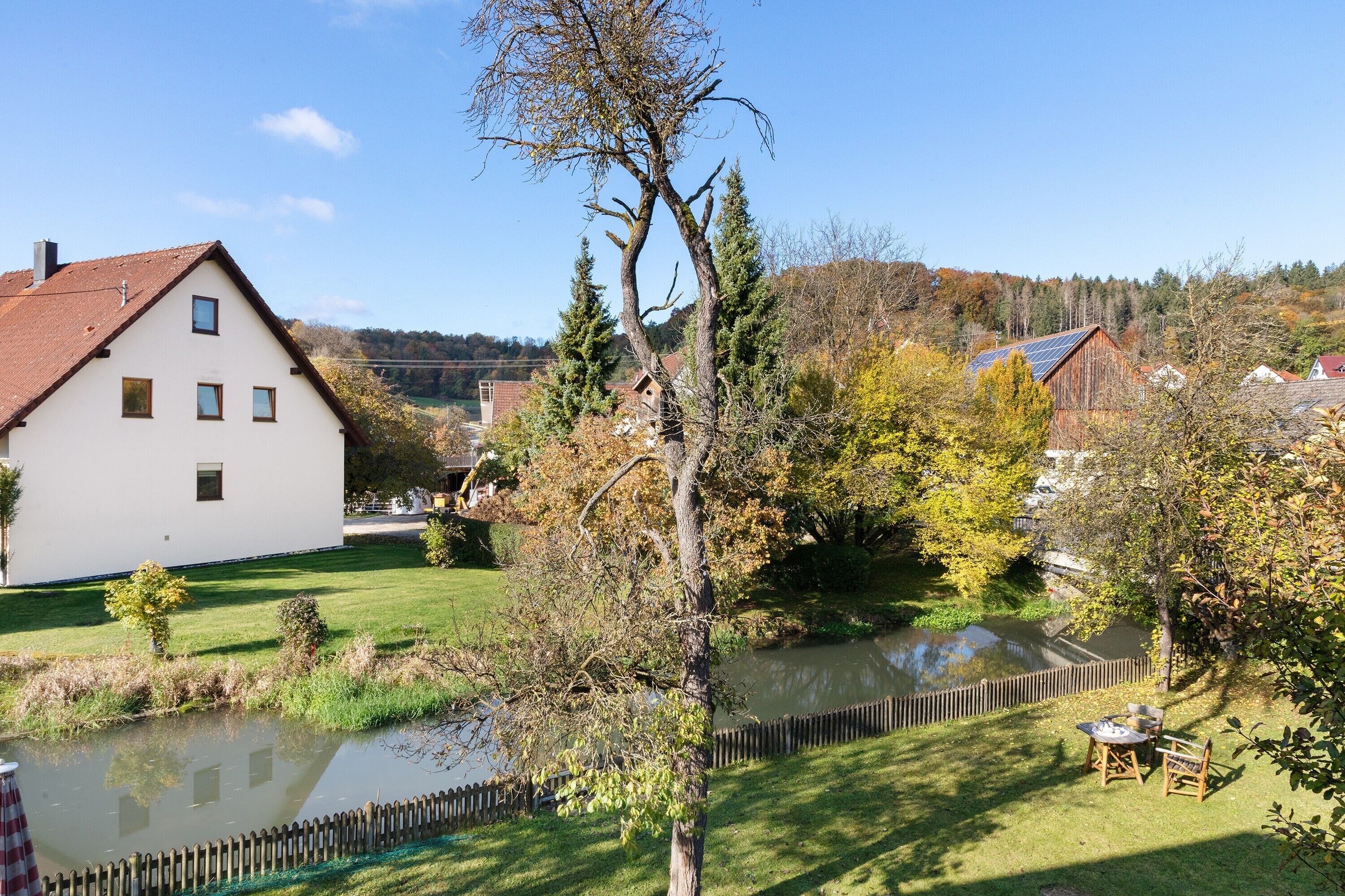 Ein weißes Gebäude mit einem geneigten Dach, einem Teich und einem Holzzaun.