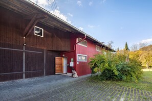 Un edificio rojo con puerta y ventanas de madera, un camino de entrada pavimentado y un árbol en primer plano.