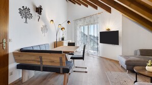 Un espace de vie moderne comprenant un coin repas, un canapé, un téléviseur fixé au mur et un plafond en bois.