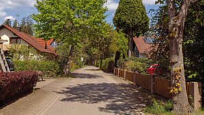 Une rue résidentielle bordée de maisons, avec une clôture en bois et une voiture rouge garée sur le côté.
