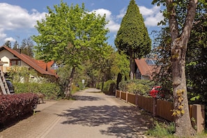 A residential street with houses, a red car, and a tree-lined path.