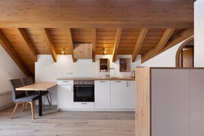 A modern kitchen with wooden beams, white cabinets, a black oven, and a dining table with chairs.