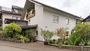 A two-story house with a number 20 on the side, a balcony with plants, and a paved driveway. - Apartment 'Zapf' with Shared Terrace, Shared Garden and Wi-Fi (Forbach)