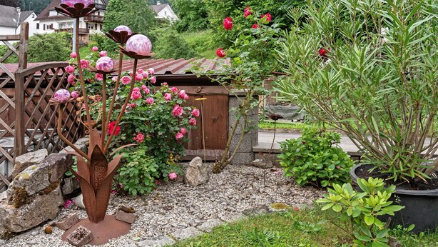 A garden with a metal sculpture, pink roses, and a wooden fence. - Apartment 'Zapf' with Shared Terrace, Shared Garden and Wi-Fi (Forbach)