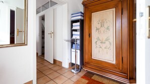 A hallway with a large wooden cabinet, a metal rack with folded towels, and a tiled floor. - Apartment 'Mengeler' with Private Terrace, Private Garden and Wi-Fi (Freiburg im Breisgau)