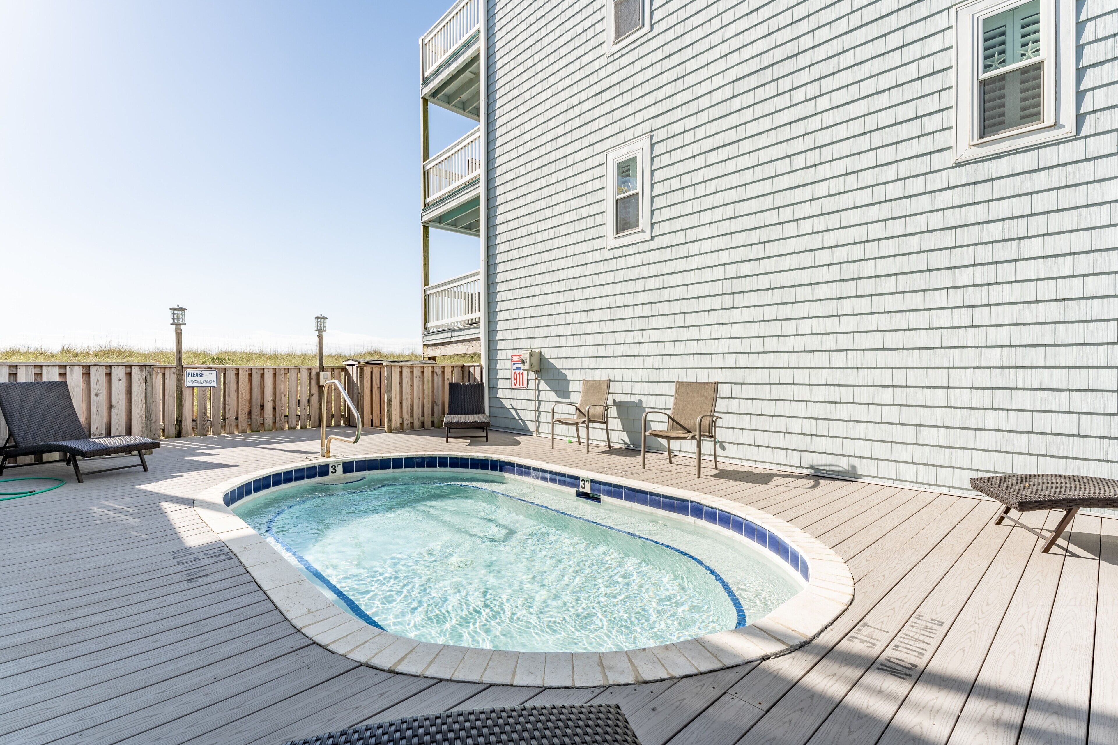 A swimming pool with a wooden deck, lounge chairs, and a wooden fence.