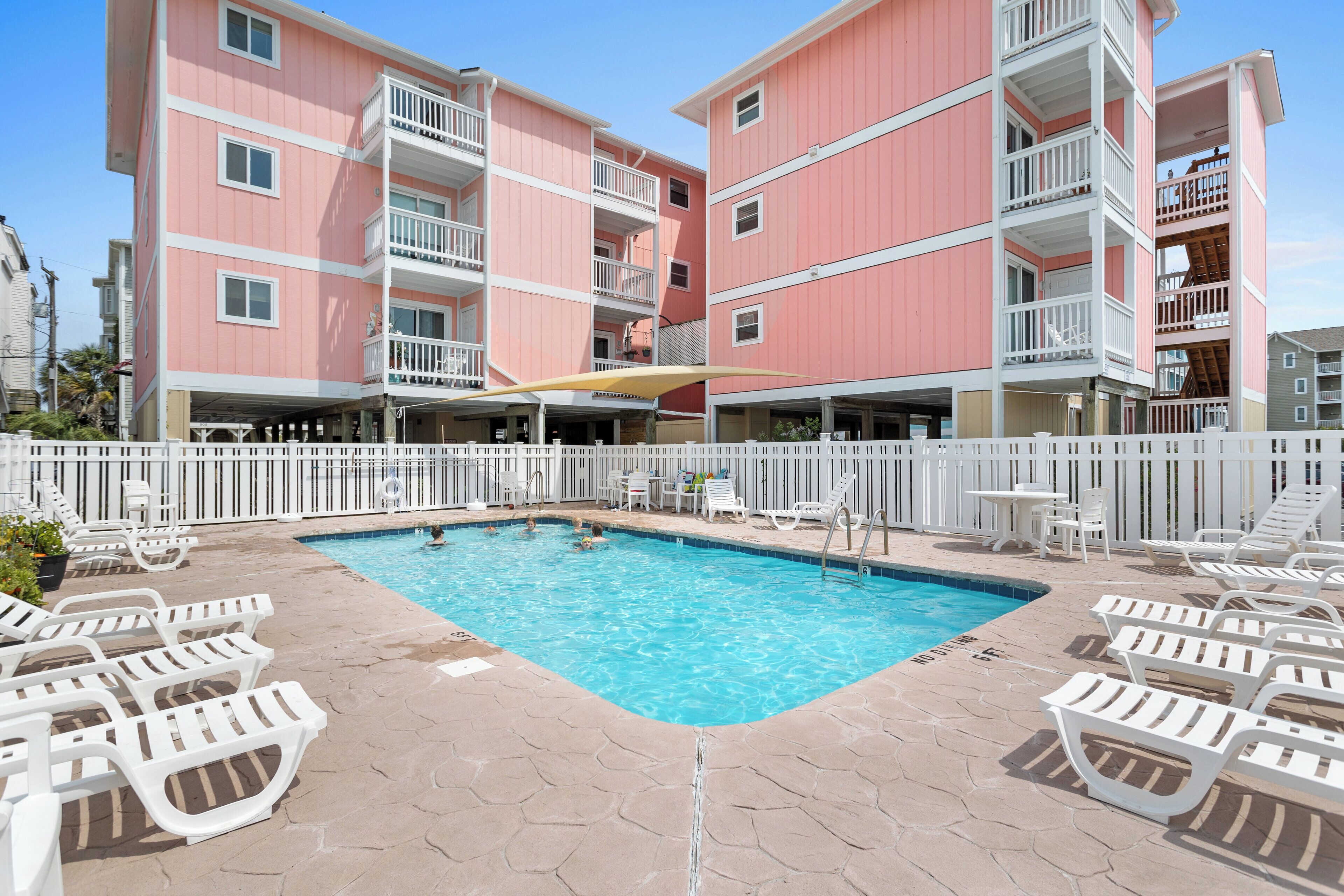 A swimming pool with lounge chairs and a white fence.