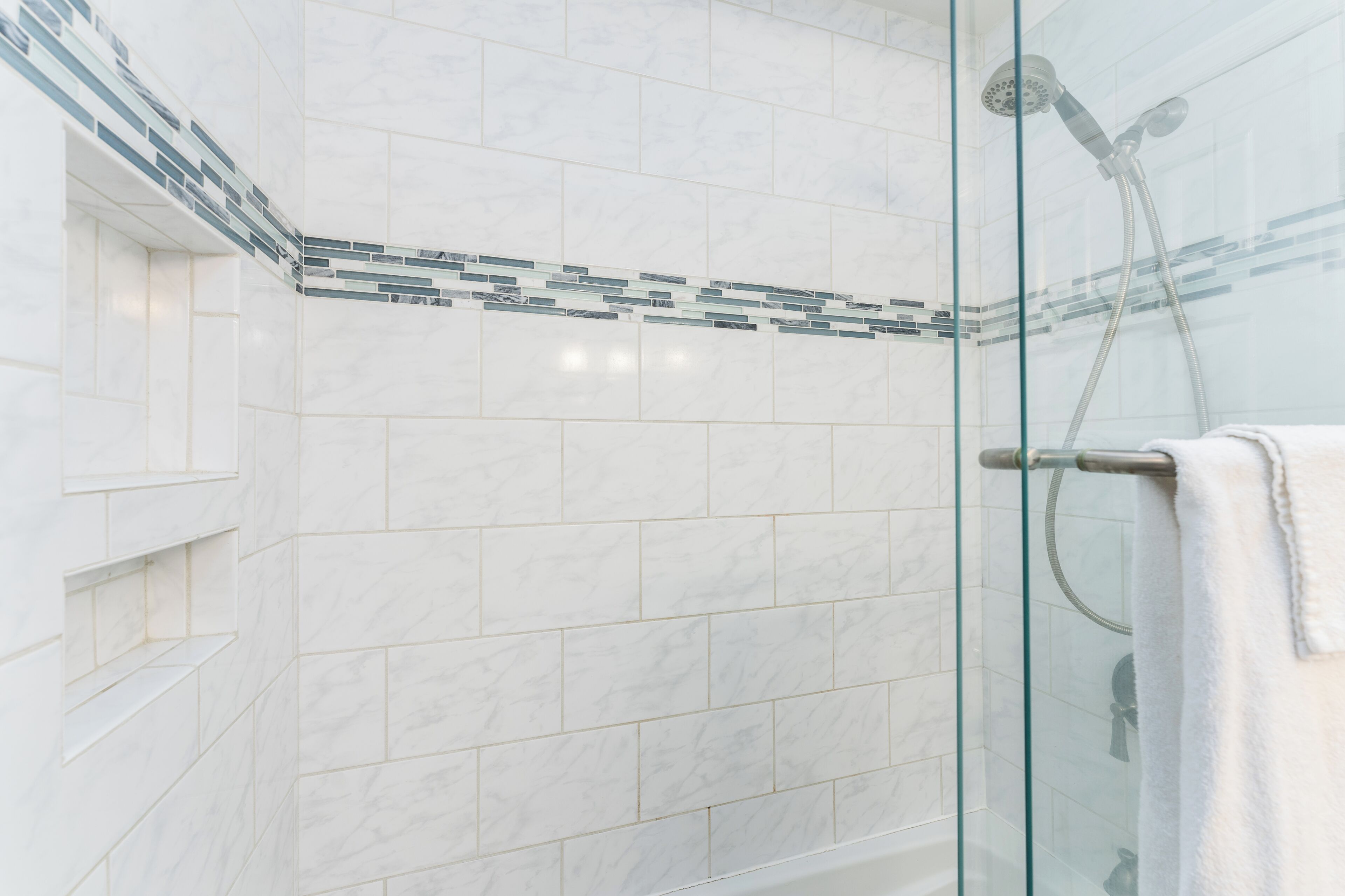 A glass-enclosed shower with a white tiled wall and a glass shower door.