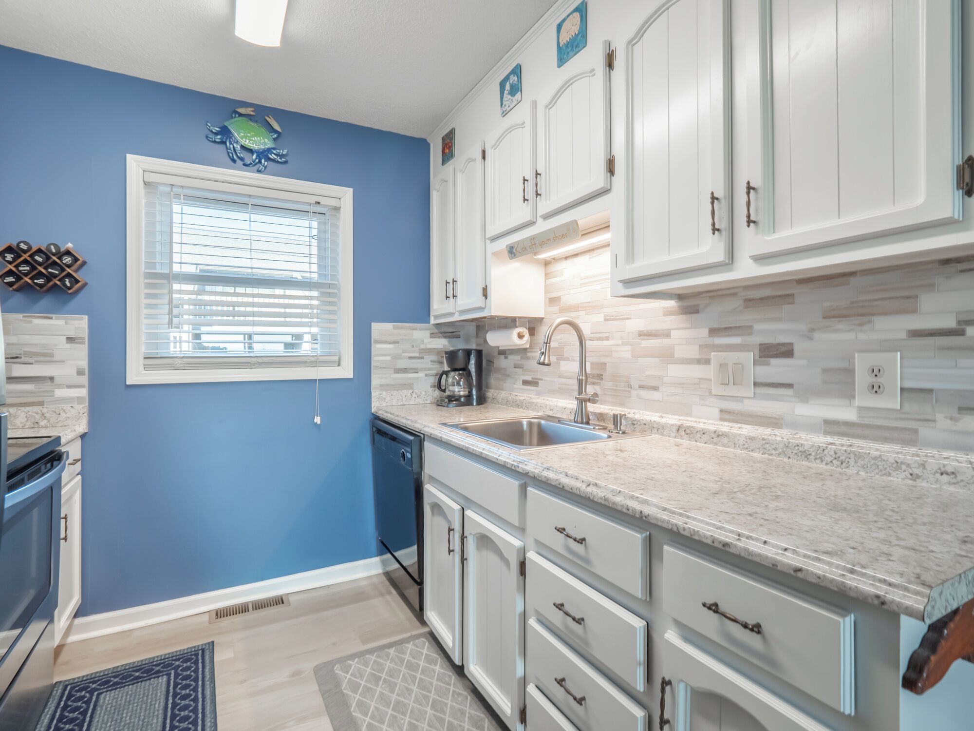 A kitchen with white cabinets, a stainless steel sink, and a window with blinds.