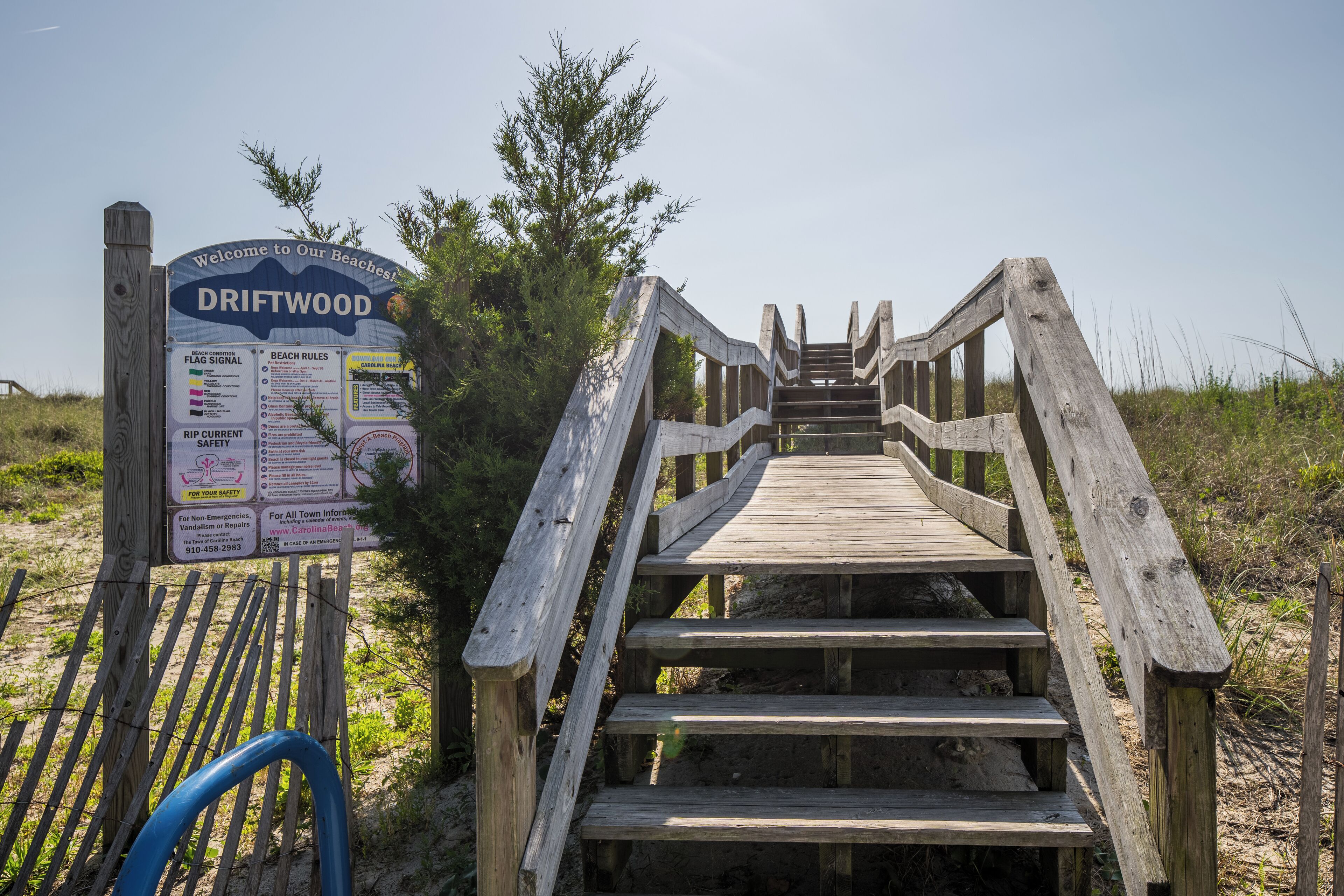 A wooden staircase leading to a beach area with a signboard displaying beach rules and safety information.
