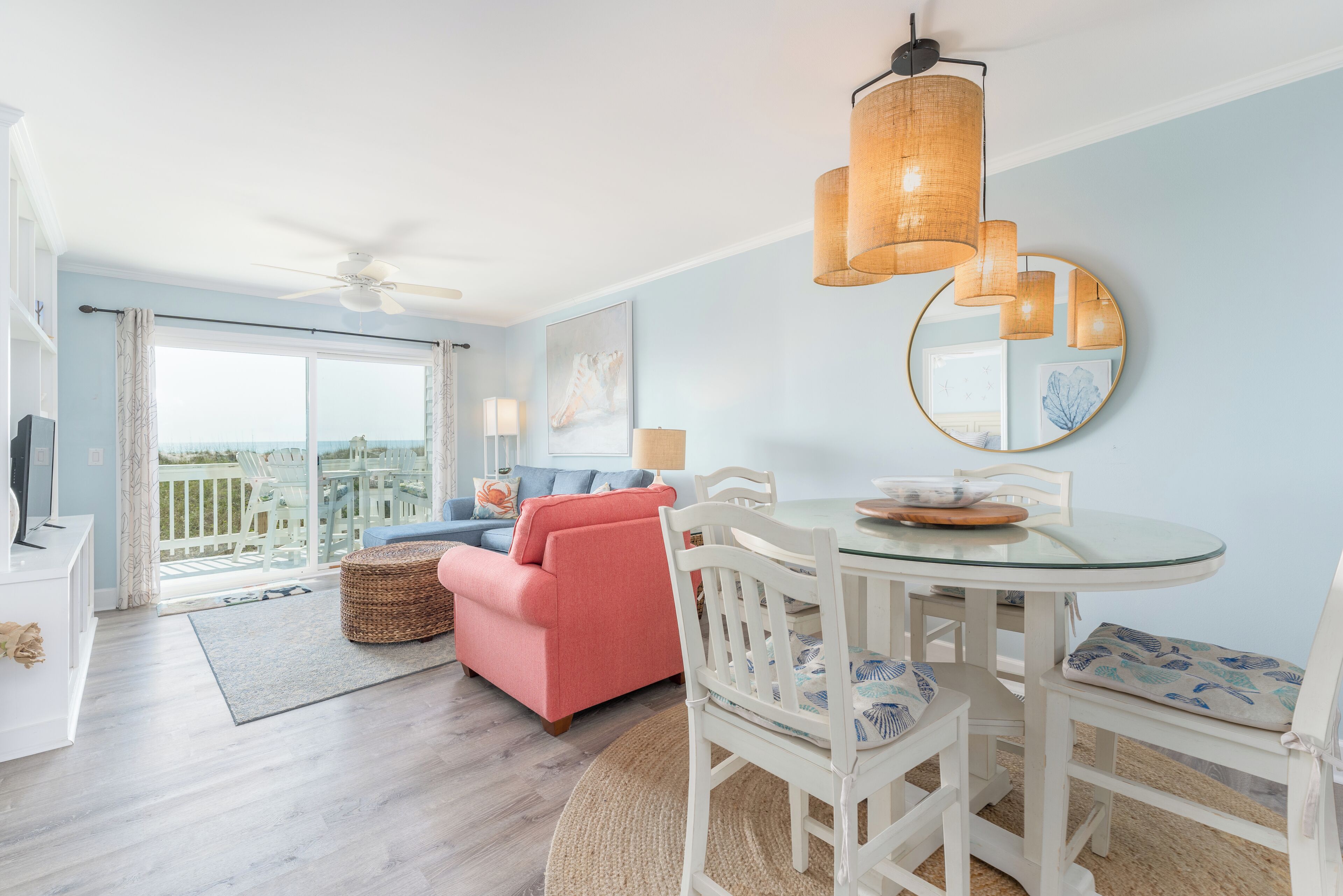 Een moderne woonkamer met een glazen eettafel, witte stoelen, een roze bank en een plafondventilator.