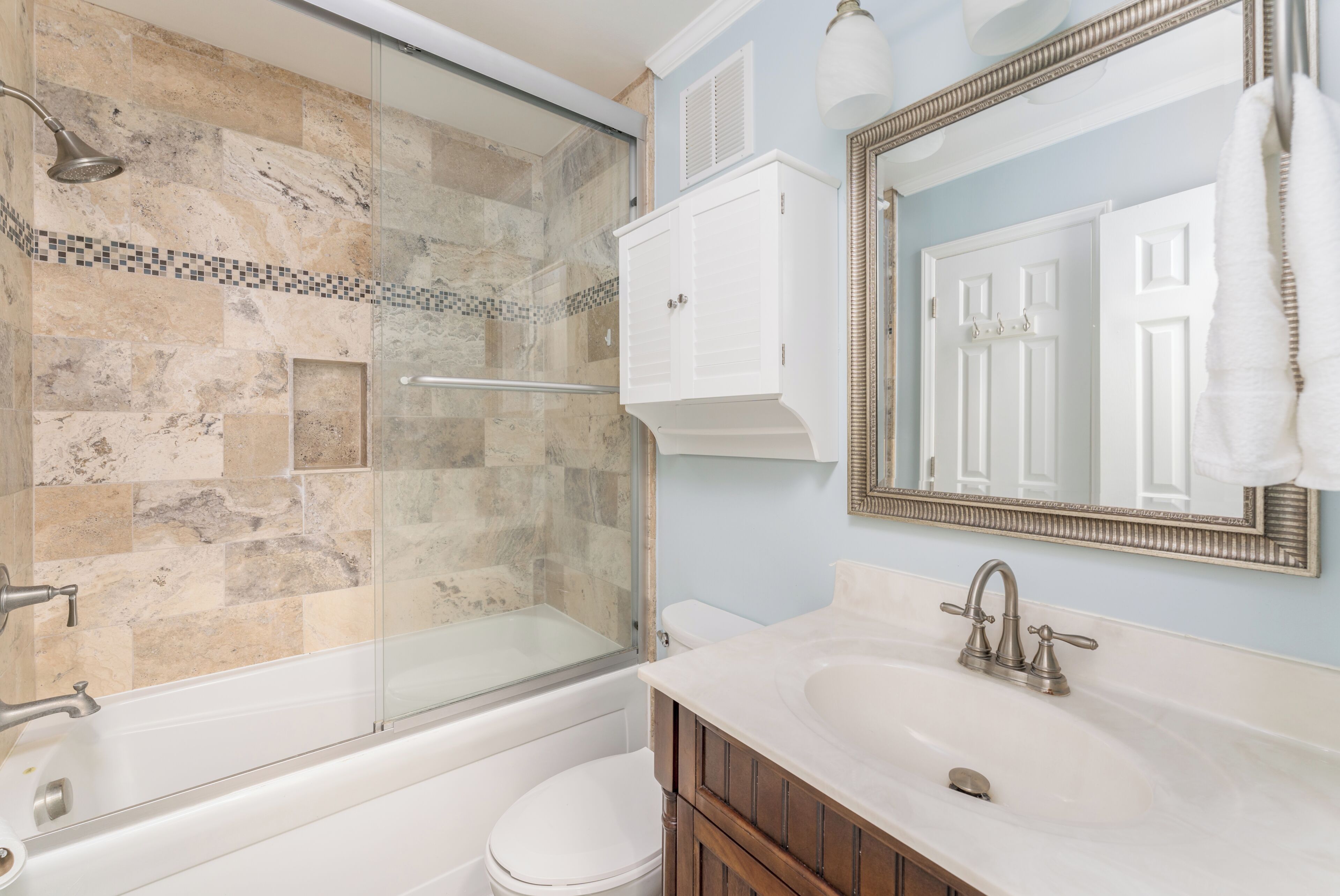 A bathroom with a glass-enclosed shower, a white toilet, a sink with a mirror, and a cabinet.