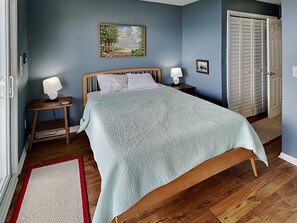 A bedroom with a bed, nightstands, a painting, and a closet. - Pelican Nest by Topsail Realty (Sneads Ferry)