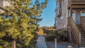 A wooden pathway leading to a building with a balcony and a staircase. - Pelican Nest by Topsail Realty (Sneads Ferry)