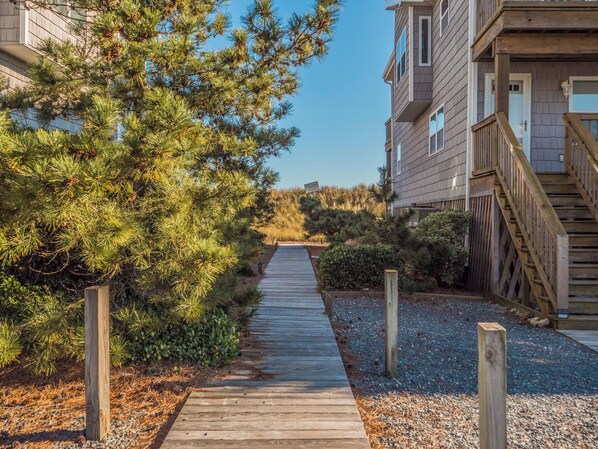 A wooden pathway leading to a building with a balcony and a staircase. - Pelican Nest by Topsail Realty (Sneads Ferry)