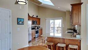 Una cocina moderna con armarios de madera, una isla grande con taburetes y un tragaluz sobre la zona de comedor.