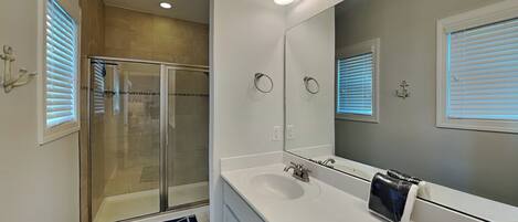 A modern bathroom with a glass shower enclosure, a large mirror, and a white vanity with a sink.